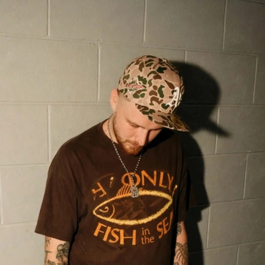 Gelapi against a cinderblock wall in a camo cap